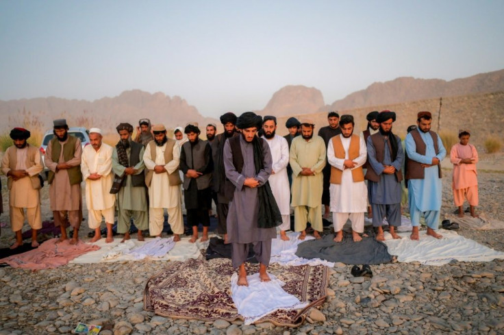 Taliban members pray together at dusk by the riverbed