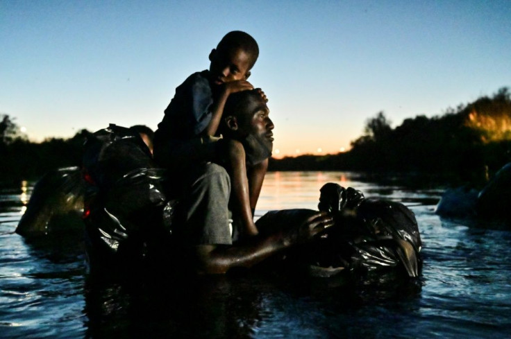 A man carries a child on his shoulders as Haitian migrants cross the Rio Grande river between Ciudad Acuna in northern Mexico and Del Rio, Texas