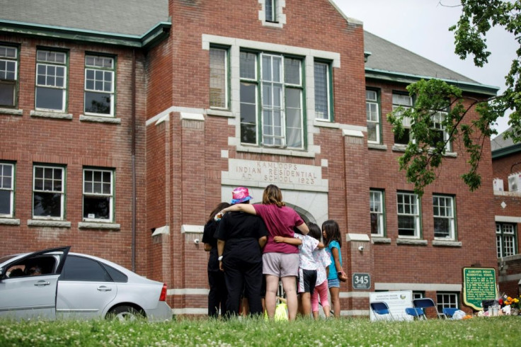 People look at the former Kamloops Indian Residential School where flowers and cards were left in June 2021 as part of a memorial to children whose remains were discovered buried near the facility