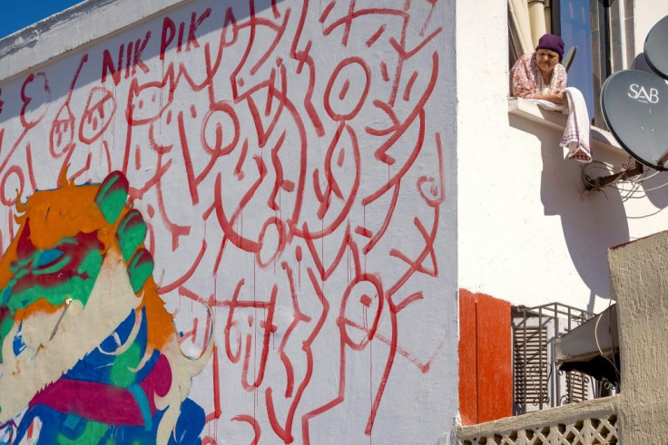 A woman looks on from her window next to a mural by Moroccan street artist Omar Lhamzi