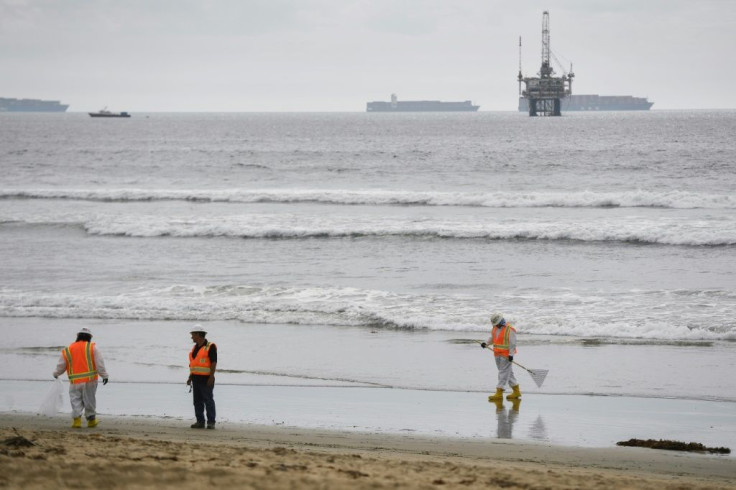 An oil platform and cargo container ships are seen on the horizon as environmental response crews clean the beach after an oil spill in the Pacific Ocean in Huntington Beach, California on October 4, 2021