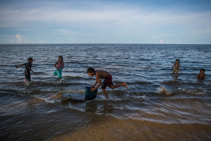 Children play on the shore of Lake Maracaibo Lake in Zulia state, Venezuela, with pieces of plastic floating on the water's surface