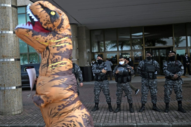 An environmental activist dressed as a dinosaur is seen in front of a line of riot police during a protest against an oil auction held in Rio de Janeiro on October 07, 2021