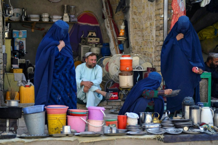 Burqa-clad women look at secondhand household items at a stall in a market in Kandahar