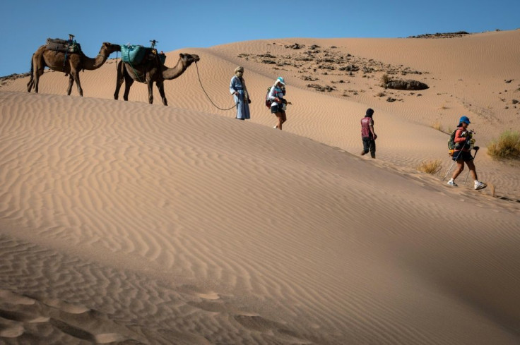 Competitors run past a camel caravan during the 35th edition of the Marathon des Sables in the southern Moroccan Sahara on October 8, 2021. Morocco depends heavily on visitors to its coastal resorts and historic inland cities