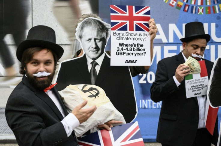 An activist dressed as a "debt collector" holds a cutout of British Prime Minister Boris Johnson during a demonstration in front of IMF headquarters to ask rich nations to help poor countries tackle climate change in Washington on October 13, 2021