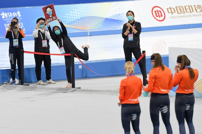 A staff member holds a sign reminding skaters to put on their face masks during a medal ceremony