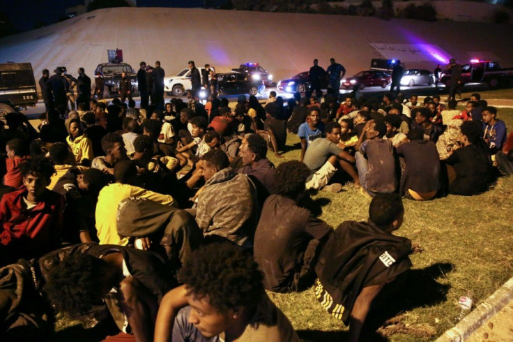 Migrants sit on the ground after being recaptured by Libyan security forces following an escape attempt