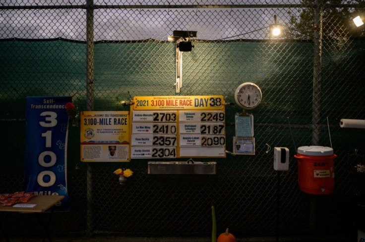 A scoreboard is displayed on a school fence showing the runners and number of miles during the 'Self-Transcendence 3100 Mile Race' on October 12, 2021