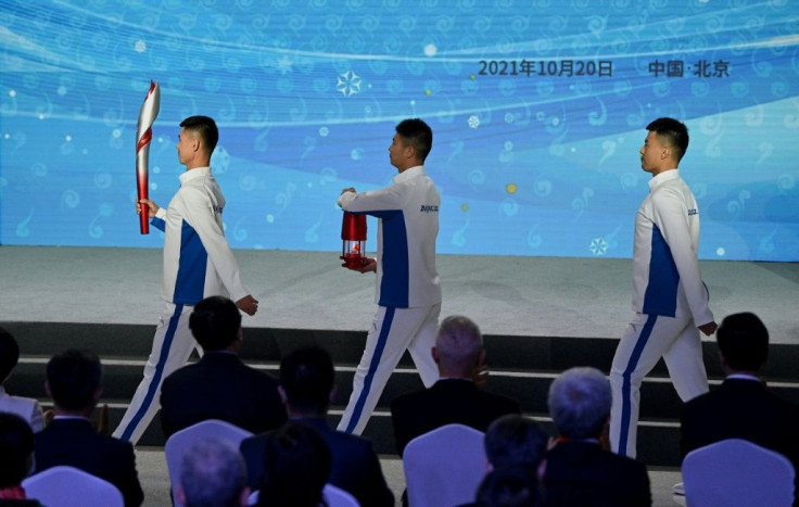 Torchbearers in white tracksuits carry a red safety lantern containing the Olympic flame