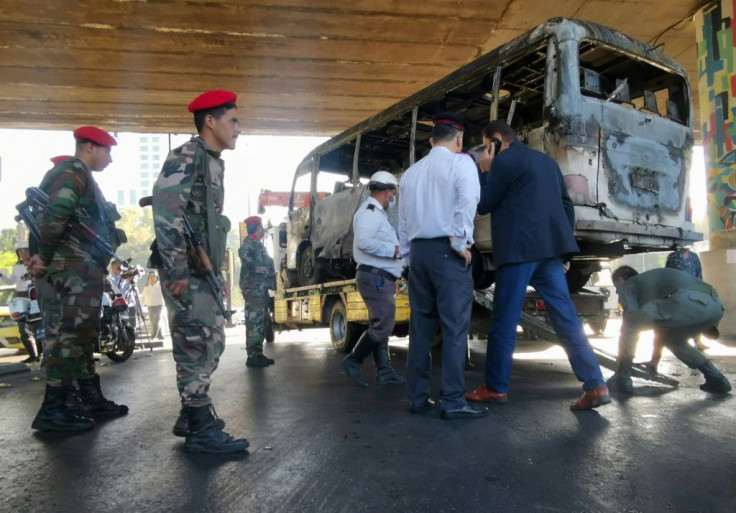 Syrian troops stand guard as investigators inspect the charred carcass of the bombed out bus