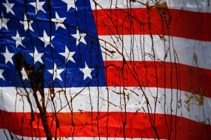 A US flag is stained with a biodegradable substance masquerading as "oil" by demonstrators with Extinction Rebellion XR Youth Los Angeles during a protest against climate change and the Line 3 oil pipeline project outside of the US Federal Building on Aug