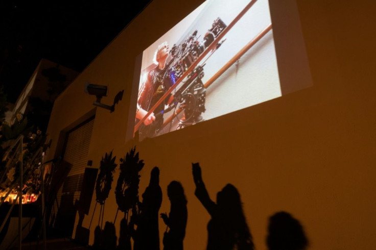 A photo of cinematographer Halyna Hutchins is seen above the shadows of people approaching a memorial table during a candlelight vigil after she was killed by a prop gun fired by actor Alec Baldwin