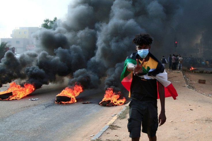 A Sudanese protester draped in the national flag flashes a V-for-victory sign next to burning tyres at a demonstration in Khartoum