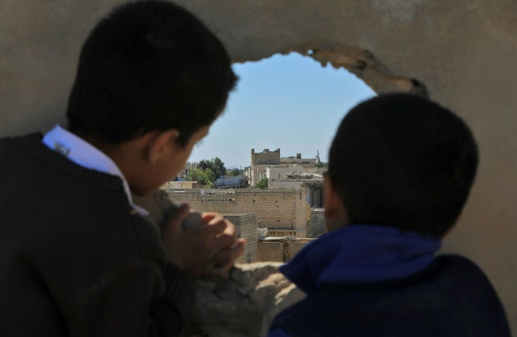 Syrian boys look through a hole on the dividing line between regime and rebel-held territory