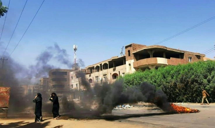 Sudanese women walk in front of tyres set ablaze by anti-coup demonstrators in the capital Khartoum, on November 7, 2021