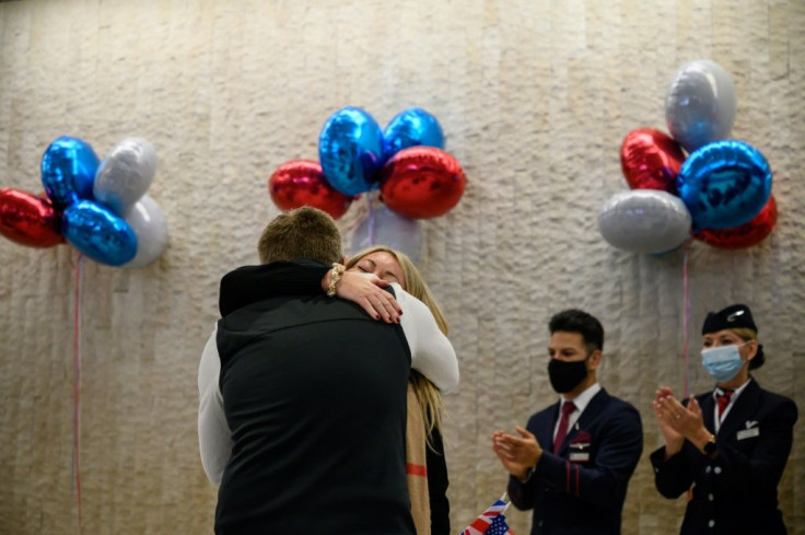 A couple embraces as they stand in front of airline staff after arriving on a flight from the UK, following the easing of pandemic travel restrictions at JFK international airport in New York on November 8, 2021