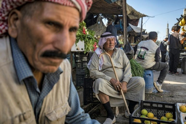 Men sit by a produce stall at a market in the centre of Syria's northern city of Raqa on November 6, 2021