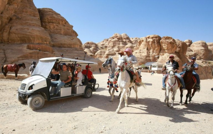 Jordanian men ride horses as tourists ride an electric cart in Jordan's famed ancient city of Petra