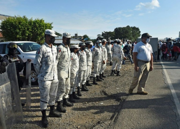 Mexican police and the National Guard wait by the side of the road as a migrant caravan passes