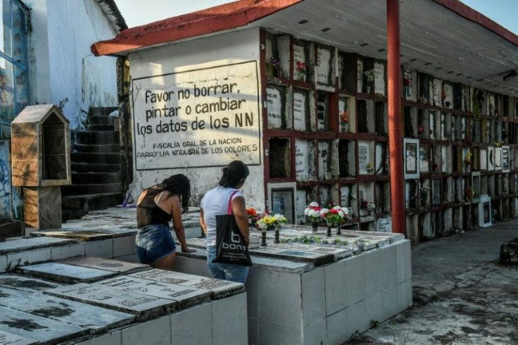 Mourners next to a sign reading: 'Please do not erase, paint or change the data of the NN' at La Dolorosa Cemetery in Puerto Berrio