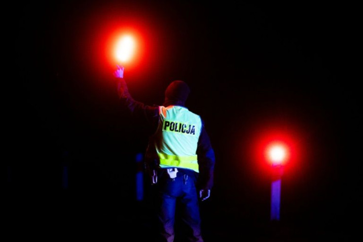 A police officer holds up a light to check vehicles at a checkpoint near the village of Bialowieza, eastern Poland, close to the Polish-Belarusian border, on November 21, 2021