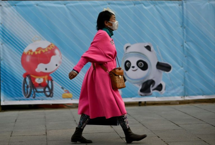 A woman walks past a poster showing the mascots of the Beijing 2022 Olympic and Paralympic Winter Games in Beijing on December 5, 2021