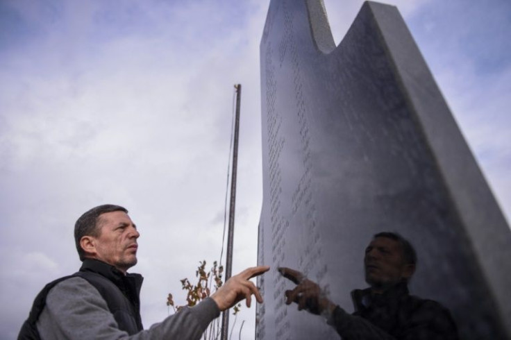 Vesel Rukolli points to the name of his father on a memorial plaque in the village of Rezalle