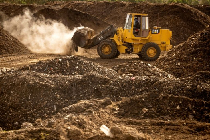 Mountains of sawdust, palettes and fruit tree branches cover a storage platform as trucks rumble past loaded with manure, and excavators aerate piles of compost