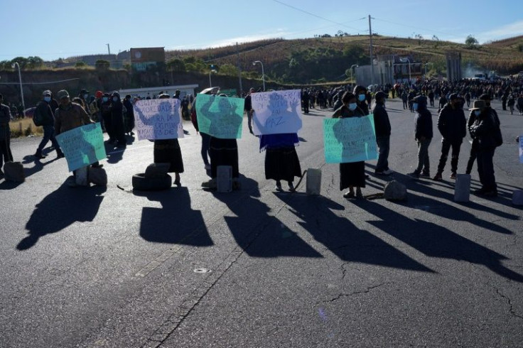 Women hold signs as they block a road during a ceremony in tribute to those killed in the weekend incident in the Guatemalan village of Chiquix