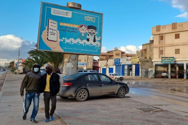 Workers on December 14, 2021 pass a billboard reading in Arabic "register and vote before missing your chance" -- but the ballot was later postponed