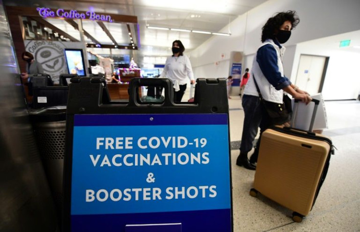 Travelers walk past a sign offering free Covid-19 vaccinations and booster shots at a pop-up clinic in the international arrivals area of Los Angeles International Airport