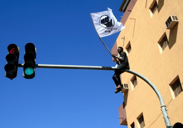 A Sudanese demonstrator sits atop a traffic light as thousands protest against the army in the capital Khartoum on December 30