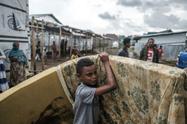 An internally displaced boy moves mattresses received from an aid organization as rain falls in July 2021 at a camp in the town of Azezo, Ethiopia for people uprooted by fighting in Tigray