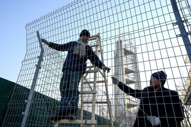 Workers use zip ties to lock up a fence to help create a "bubble" surrounding the Beijing Olympic Park
