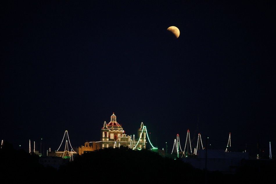 A partial lunar eclipse is seen over the village of Zejtun, lit up for its parish church feast of Saint Catherine, in the south of Malta