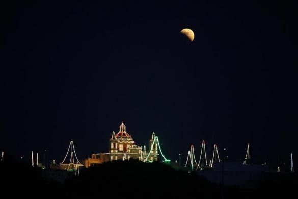 A partial lunar eclipse is seen over the village of Zejtun, lit up for its parish church feast of Saint Catherine, in the south of Malta June 15, 2011.