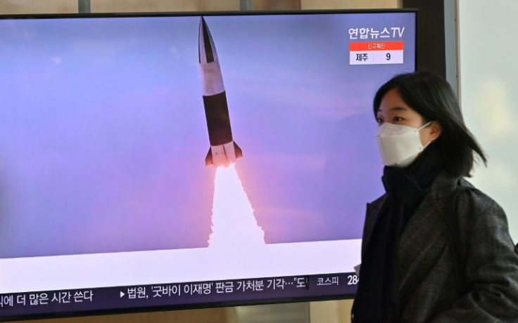 A woman walks past a television screen showing a news broadcast with file footage of a North Korean missile test, at a railway station in Seoul on January 20, 2022