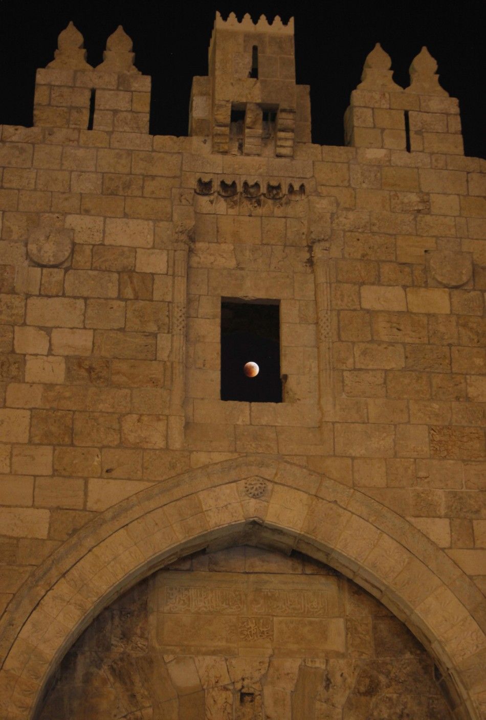 The moon is seen behind the wall of Damascus gate in Jerusalem old city during a total lunar eclipse