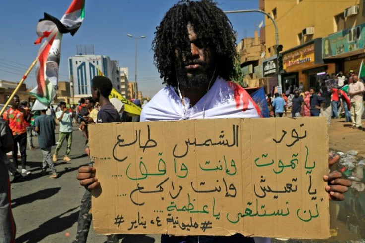 A Sudanese protester carries a placard which reads in Arabic, "the sun is shining, either die on your feet or live on your knees, we won't lie down"