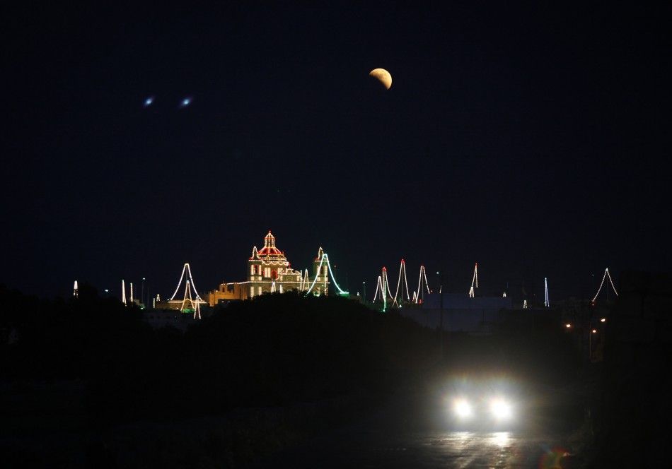 A partial lunar eclipse is seen over the village of Zejtun, lit up for its parish church feast of Saint Catheri