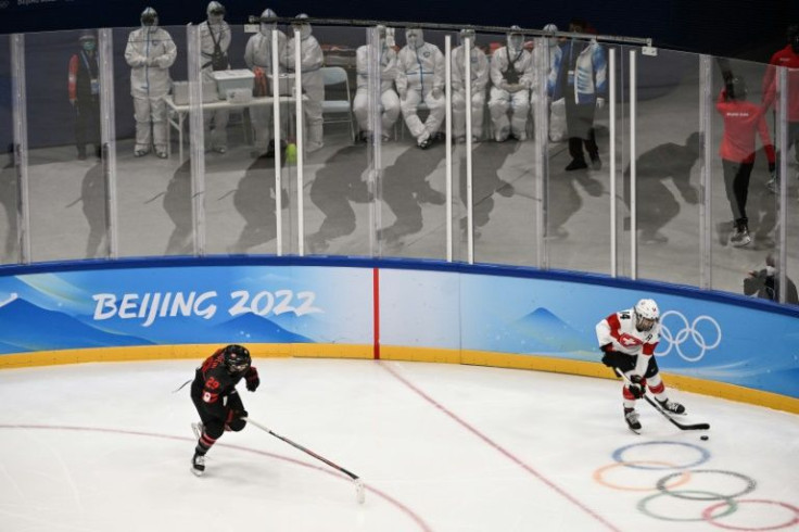 Games personnel in protective equipment watch a women's ice hockey game between Canada and Switzerland