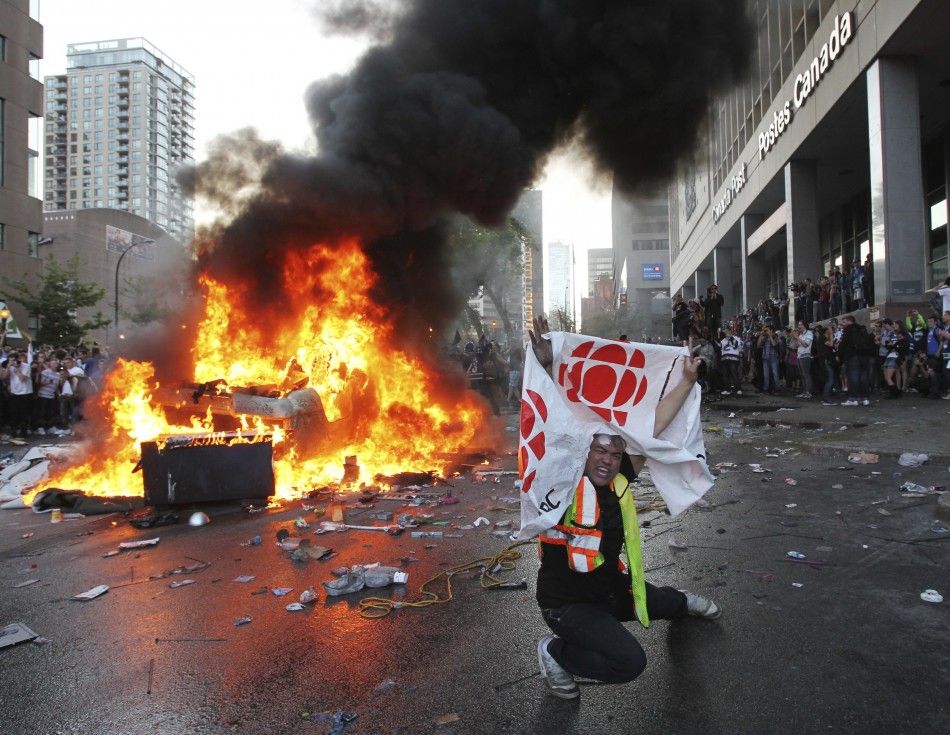 A Canucks fan waves in front of an overturned burning pickup truck in downtown Vancouver, British Columbia during riots after the Canucks lost the NHL Stanley Cup playoffs to the Bruins