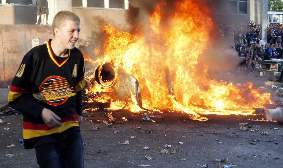 A Canucks fan stands in front of a burning vehicle during riots in Vancouver, British Columbia after the Canucks lost the NHL Stanley Cup final hockey game to the Bruins