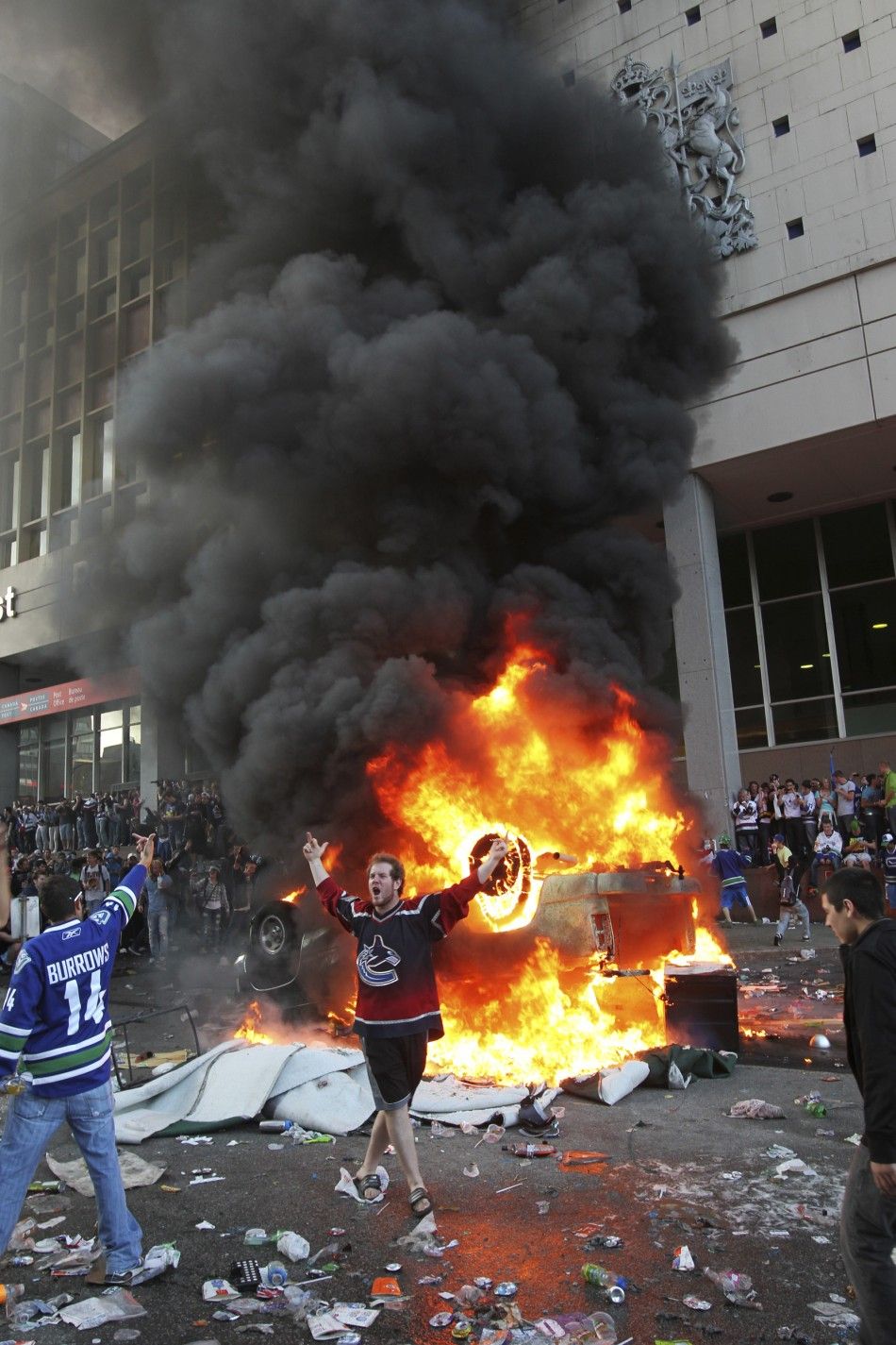 A Canucks fan gestures in front of an overturned burning pickup truck during riots in downtown Vancouver, British Columbia