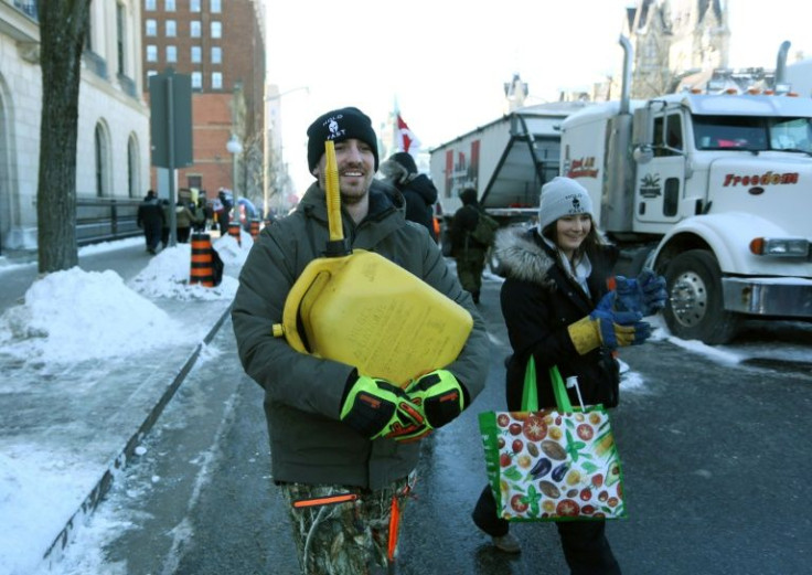 A demonstrator carries a jerry can of gasoline to a waiting truck in downtown Ottawa, Canada during a February 5, 2022 protest against Covid-19 restrictions; truckers appear to be preparing for a long stay