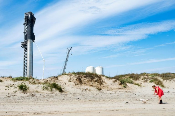 A woman walks her dog on the beach near SpaceX's first orbital Starship SN20 stacked atop its massive Super Heavy Booster 4 at the company's Starbase facility