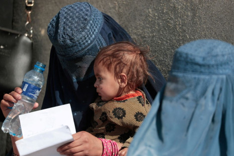 A displaced Afghan woman holds her child as she waits with other women to receive aid supply outside an UNCHR distribution center on the outskirts of Kabul, Afghanistan October 28, 2021. 