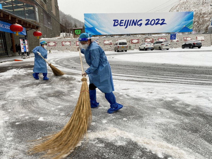 Volunteers wearing personal protective equipment (PPE) clear away snow with straw brooms outside the Zhangjiakou media centre, during a snowfall at the Winter Olympics, in Zhangjiakou, China, February 12, 2022.