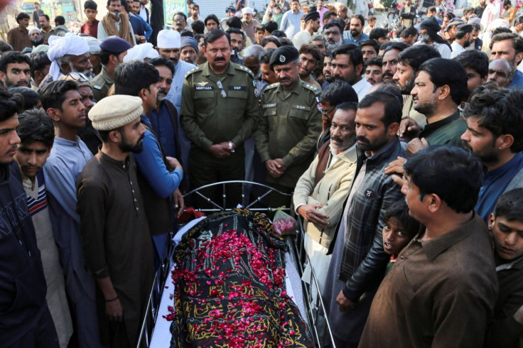 People stand beside the body of a man, who according to the police, was lynched by a mob for allegedly burning pages of Muslim holy book, "The Koran" in Tulamba Village, in Mian Channu, Pakistan, February 13, 2022. 